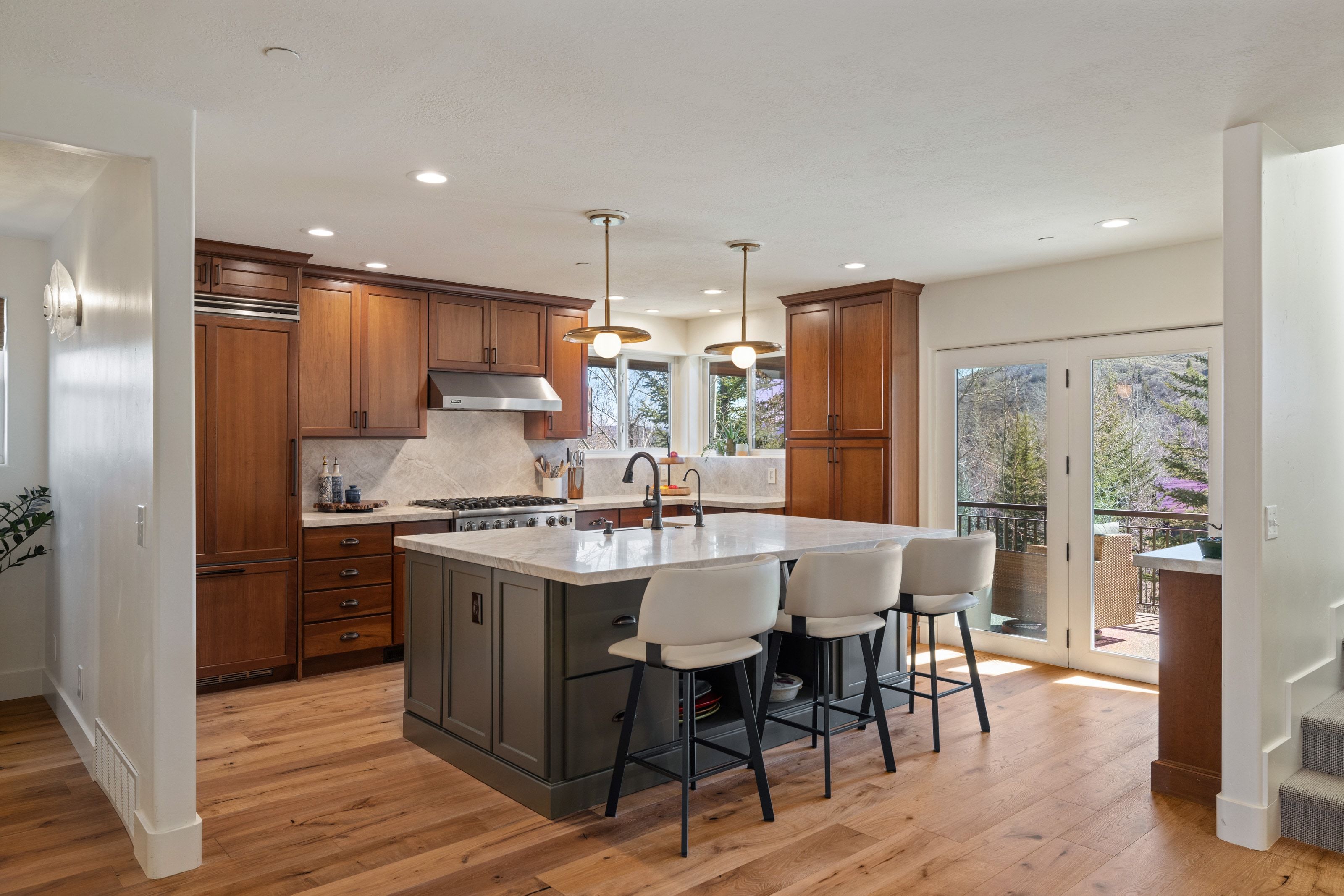 Kitchen with a kitchen breakfast bar, an island with sink, decorative light fixtures, light stone counters, and wood finish cabinets