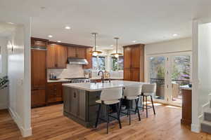 Kitchen with a kitchen breakfast bar, an island with sink, decorative light fixtures, light stone counters, and wood finish cabinets