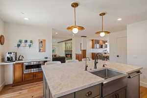 Dual tone kitchen with a fireplace, light wood finished floors, an island with sink, hanging light fixtures, and stainless steel appliances