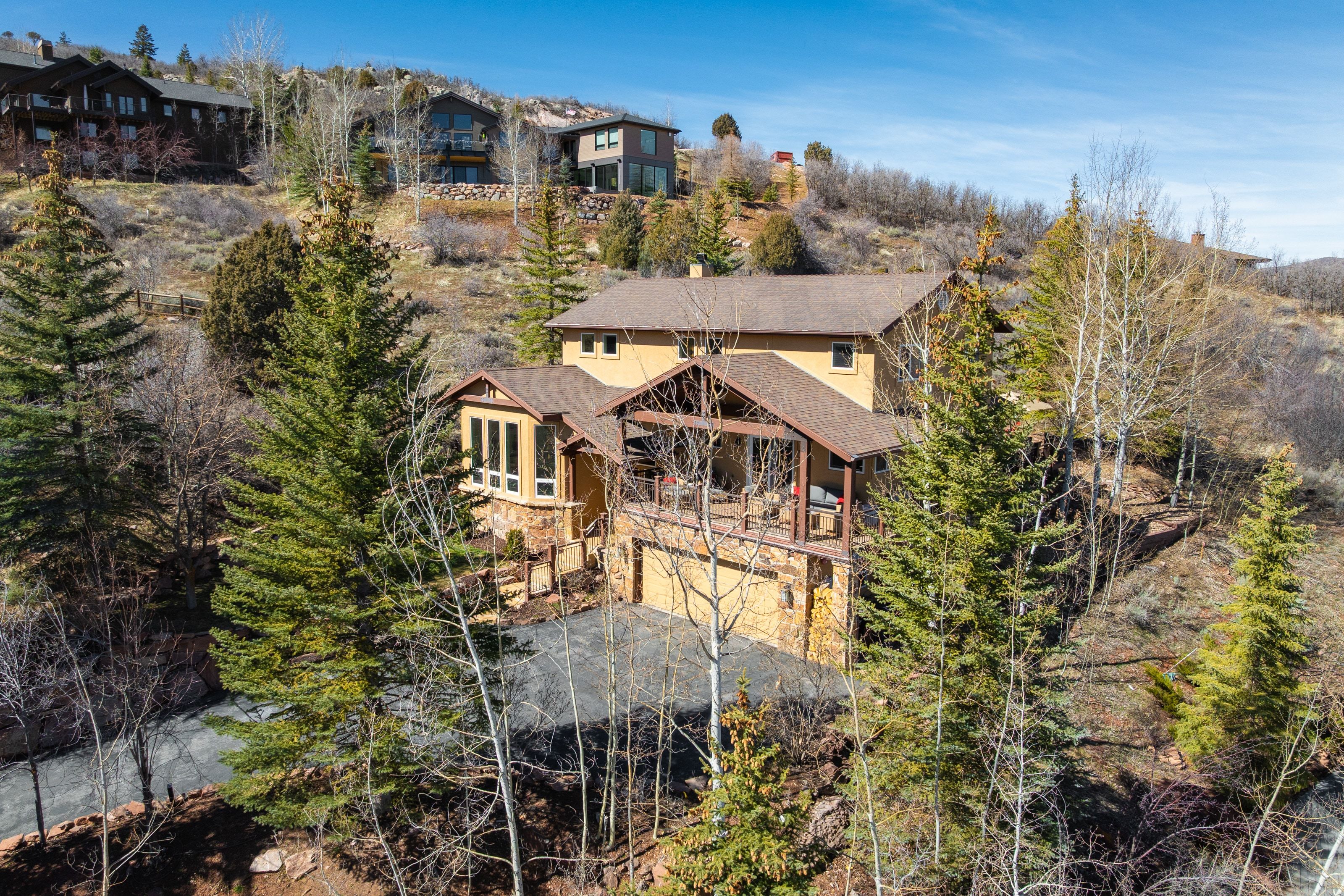 Back of house with an attached garage, driveway, a balcony, and view of wooded area