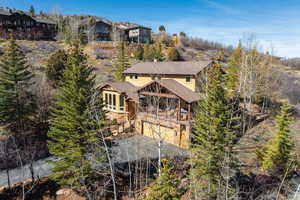 Back of house with an attached garage, driveway, a balcony, and view of wooded area