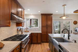 Kitchen with stainless steel stove, light wood-style floors, wood finish cabinets, pendant lighting, and decorative backsplash