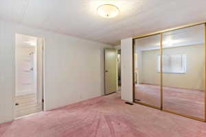 Unfurnished bedroom featuring light colored carpet, a closet, a textured ceiling, and a decorative wall