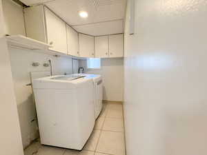 Laundry room with light tile patterned flooring, independent washer and dryer, cabinet space, and a drop ceiling