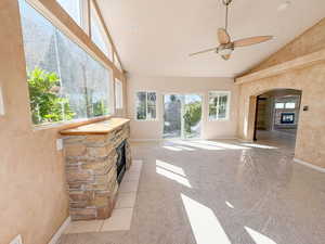 Sunroom with a fireplace, ceiling fan, lofted ceiling, light colored carpet, and arched walkways