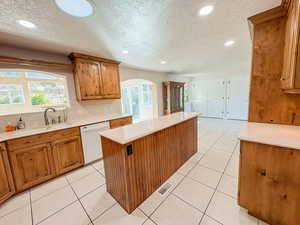 Kitchen with wood finish cabinets, a textured ceiling, a center island, decorative backsplash, and white dishwasher