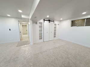 Finished great room/den area with a barn door, light colored carpet, and recessed lighting