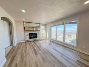 Unfurnished living room featuring recessed lighting, light wood-type flooring, a textured ceiling, arched walkways, and a stone fireplace