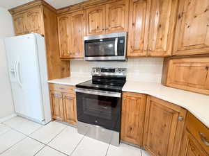 Kitchen featuring stainless steel appliances, tasteful backsplash, wood finish cabinets, and light tile patterned floors