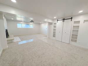 Basement with carpet, recessed lighting, built in features, a barn door, and a fireplace with raised hearth