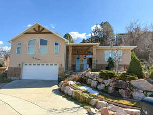 View of front of property featuring stone siding, an attached garage, driveway, and stucco siding