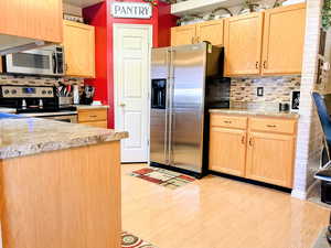 Kitchen with light wood finish cabinets, decorative backsplash, stainless steel appliances, light countertops, and light wood finished floors