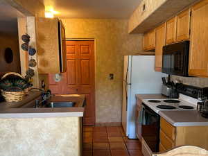Kitchen with electric range, black microwave, dark tile patterned floors, wood finish cabinets, and light countertops