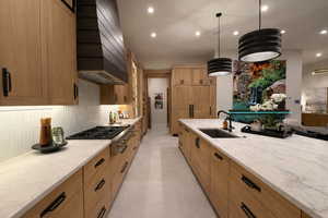 Kitchen with light stone counters, pendant lighting, stainless steel gas stovetop, and wood finish cabinetry