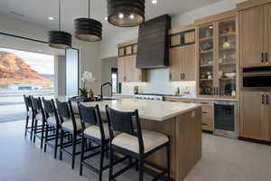 Kitchen with a kitchen breakfast bar, a large island, wine cooler, hanging light fixtures, and glass insert cabinets