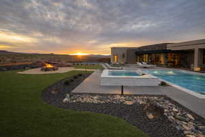 Pool at dusk featuring an outdoor fire pit, a patio area, a lawn, and a pool with connected hot tub