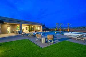 Pool at night featuring a patio, an outdoor pool, a yard, and area for grilling