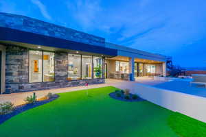 Back of house featuring an outdoor kitchen, stone siding, a patio area, an area to practice putting, and stucco siding