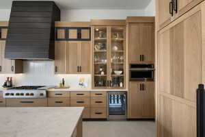 Kitchen with beverage cooler, light wood finish cabinetry, light stone counters, and white gas stovetop
