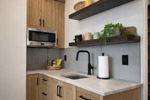 Kitchen featuring open shelves, stainless steel microwave, light wood finish cabinetry, and tasteful backsplash