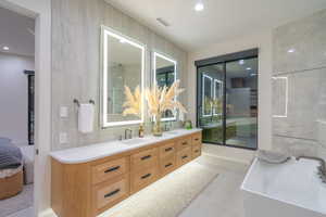 Full bathroom featuring a freestanding tub, double vanity, connected bathroom, recessed lighting, and tile walls