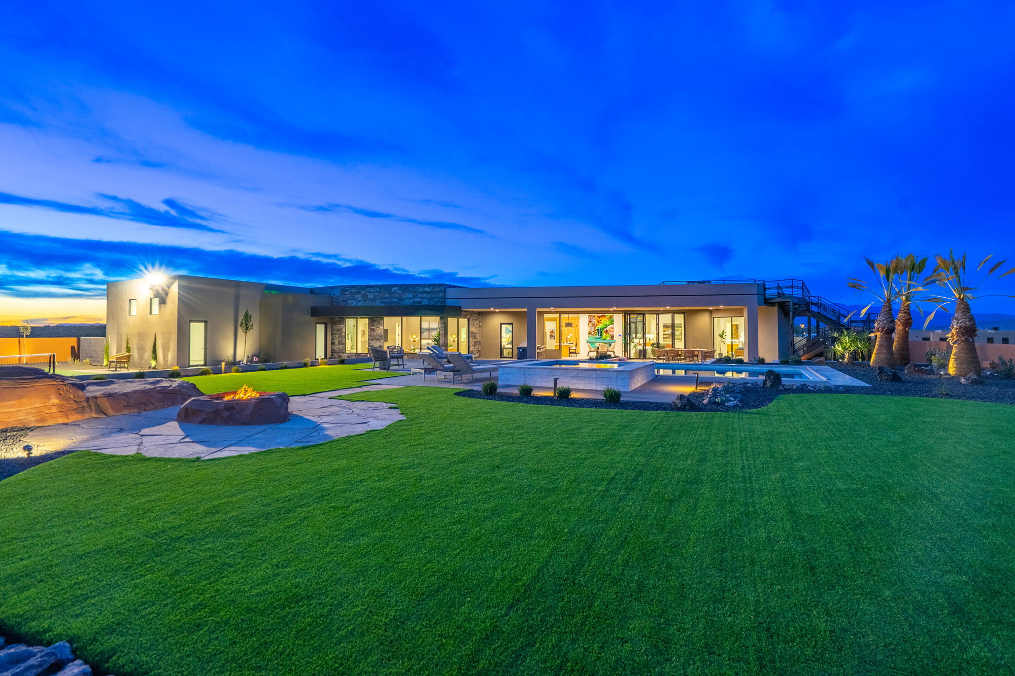 Back of property at dusk featuring a hot tub, a fire pit, an outdoor pool, and a patio