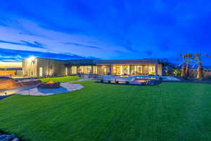 Back of property at dusk featuring a hot tub, a fire pit, an outdoor pool, and a patio