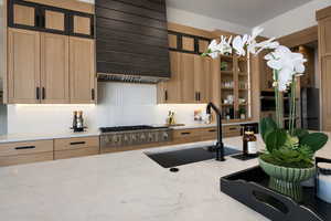 Kitchen featuring light wood finish cabinets, light stone countertops, stainless steel appliances, and glass insert cabinets