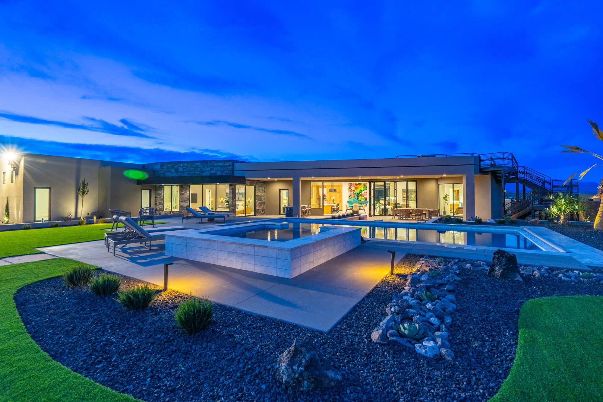 Back of house at dusk featuring a patio area, an in-ground hot tub, stucco siding, and an outdoor pool
