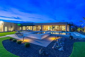 Back of house at dusk featuring a patio area, an in-ground hot tub, stucco siding, and an outdoor pool