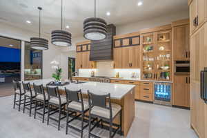 Kitchen featuring a kitchen bar, beverage cooler, a large island, hanging light fixtures, and light stone counters