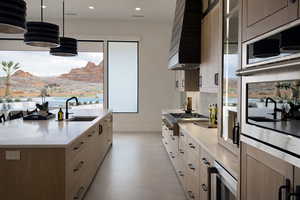 Kitchen featuring healthy amount of natural light, stainless steel appliances, decorative light fixtures, a kitchen island with sink, and two tone color scheme