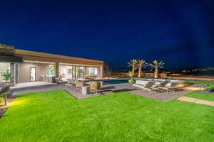 Pool at night with a patio area, an outdoor pool, and a lawn