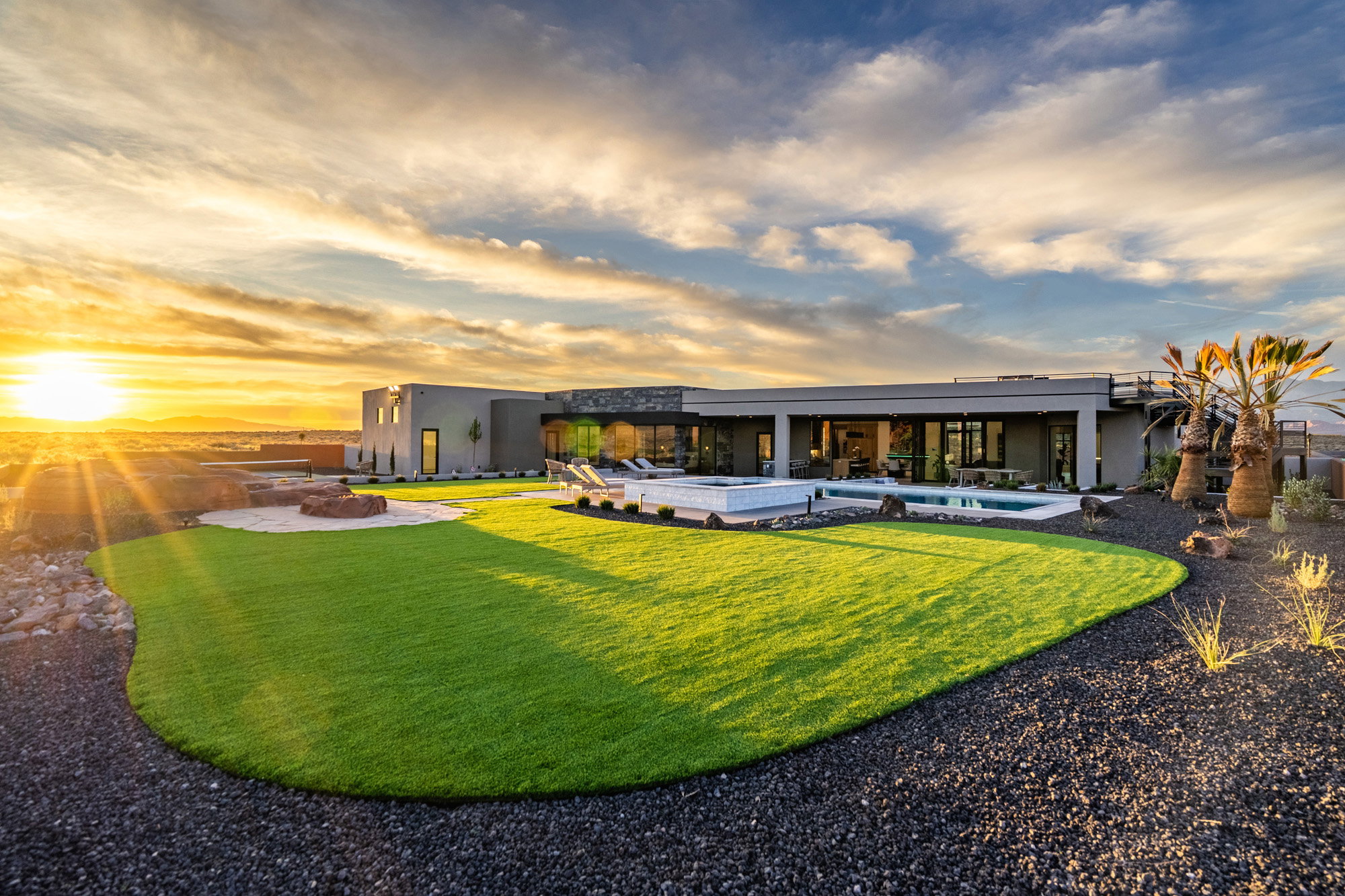 Back of house at dusk featuring stucco siding, a patio, a lawn, and a jacuzzi