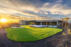 Back of house at dusk featuring stucco siding, a patio, a lawn, and a jacuzzi