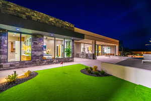 Back of house at night featuring an outdoor kitchen, an area to practice putting, a patio, and stone siding