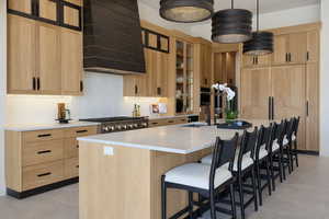 Kitchen featuring light wood finish cabinetry, a kitchen bar, a spacious island, decorative light fixtures, and light stone counters