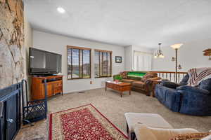 Living room with light colored carpet, suspended lighting, and a textured ceiling