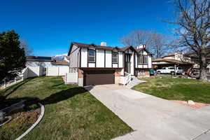 View of front of property featuring a chimney, a garage, concrete driveway, stucco siding, and brick siding