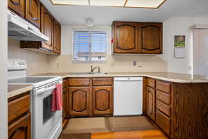 Kitchen featuring white appliances, a peninsula, light countertops, and wood finish cabinets