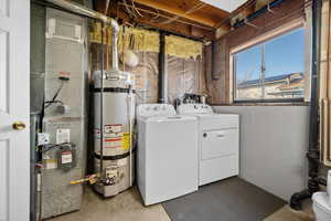 Laundry area featuring concrete floors, water heater, heating unit, and washing machine and clothes dryer