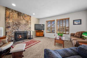 Living room featuring a stone fireplace, carpet floors, a textured ceiling, and radiator