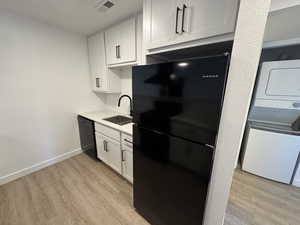 Kitchen with black appliances, white cabinets, light wood finished floors, and stacked washer / dryer