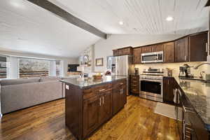 Kitchen featuring dark wood finish cabinetry, vaulted ceiling, stainless steel appliances, open floor plan, and a kitchen island