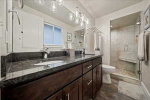 Full bath featuring double vanity, a stall shower, and dark wood-type flooring