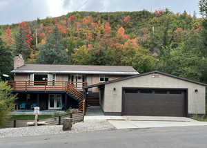 Ranch-style house featuring brick siding, a wooded view, a chimney, stucco siding, and an attached garage