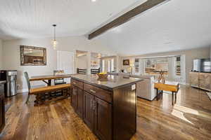 Kitchen with dark wood finish cabinets, open floor plan, dark wood-style flooring, decorative light fixtures, and a kitchen island