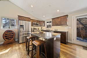 Kitchen featuring dark wood finish cabinets, stainless steel appliances, a breakfast bar, light wood-style floors, and dark stone countertops