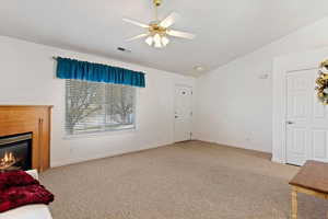 Unfurnished living room featuring light carpet, vaulted ceiling, a ceiling fan, and a glass covered fireplace
