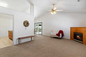 Living area featuring light colored carpet, a glass covered fireplace, a ceiling fan, and a high ceiling